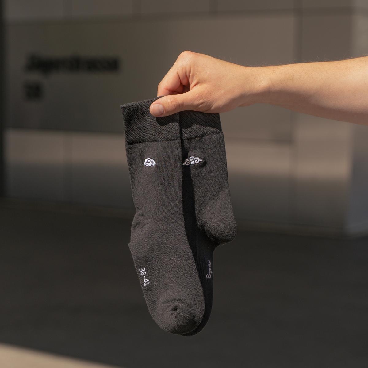 Synix Kumo 7 sustainable socks in black with white cloud embroidery held in airport