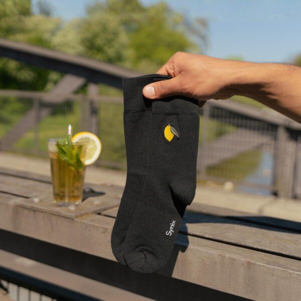 Synix Limona sustainable socks in black with lemon embroidery held outdoors