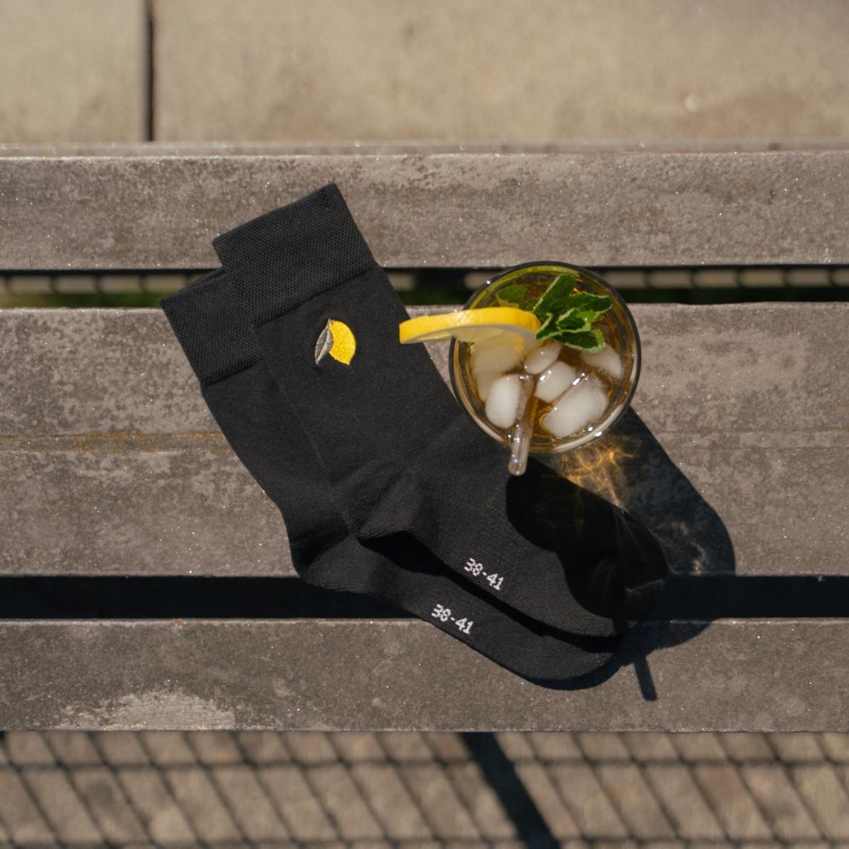 Close-up of lemon embroidery on black Synix Limona sustainable sock next to a lemonade