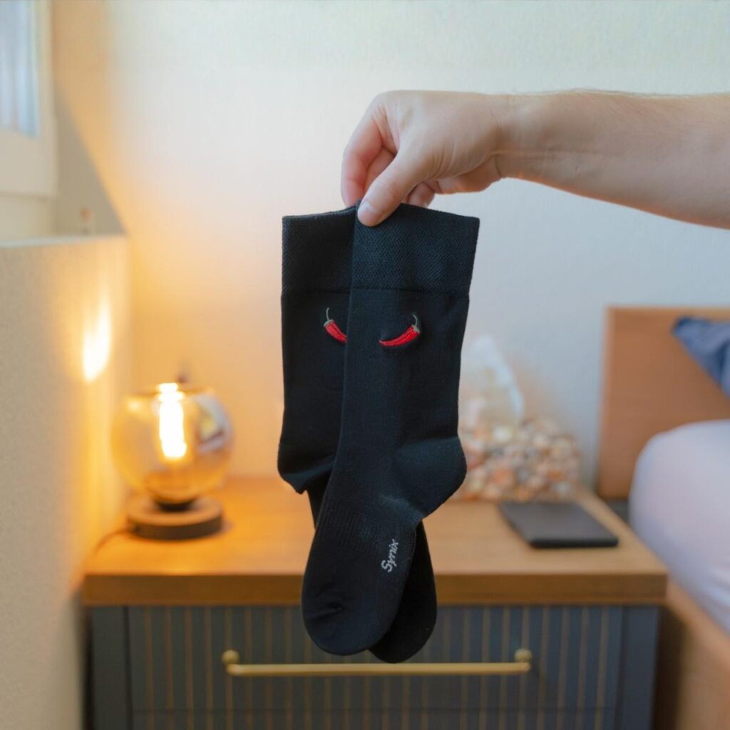 Synix Pili Pili sustainable socks in black with red chili embroidery held indoors