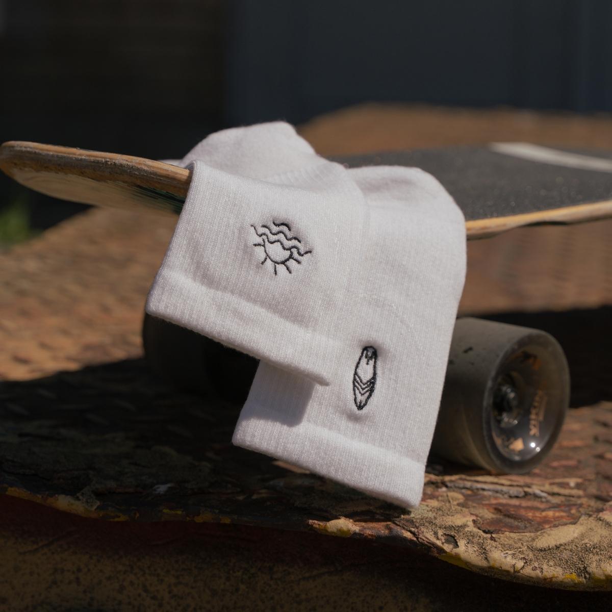 Close-up of ocean sun and surfboard embroidery on white Synix SunSeeker sustainable sock on surfskate