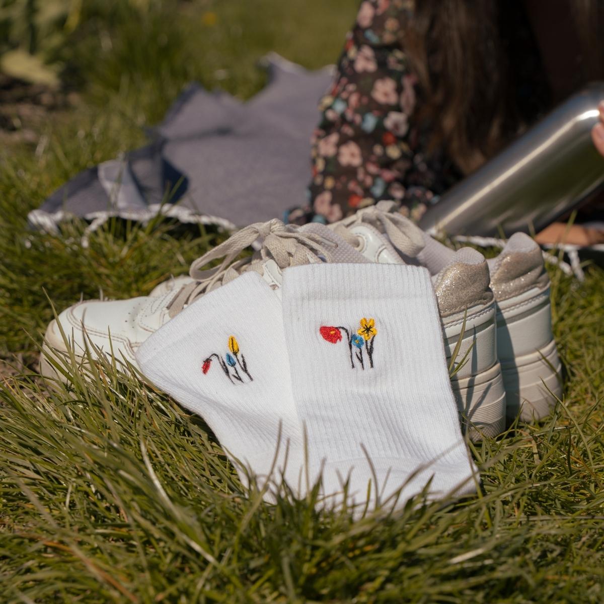 White Synix UnFold sustainable socks with tulip embroidery placed on top of shoes outdoors