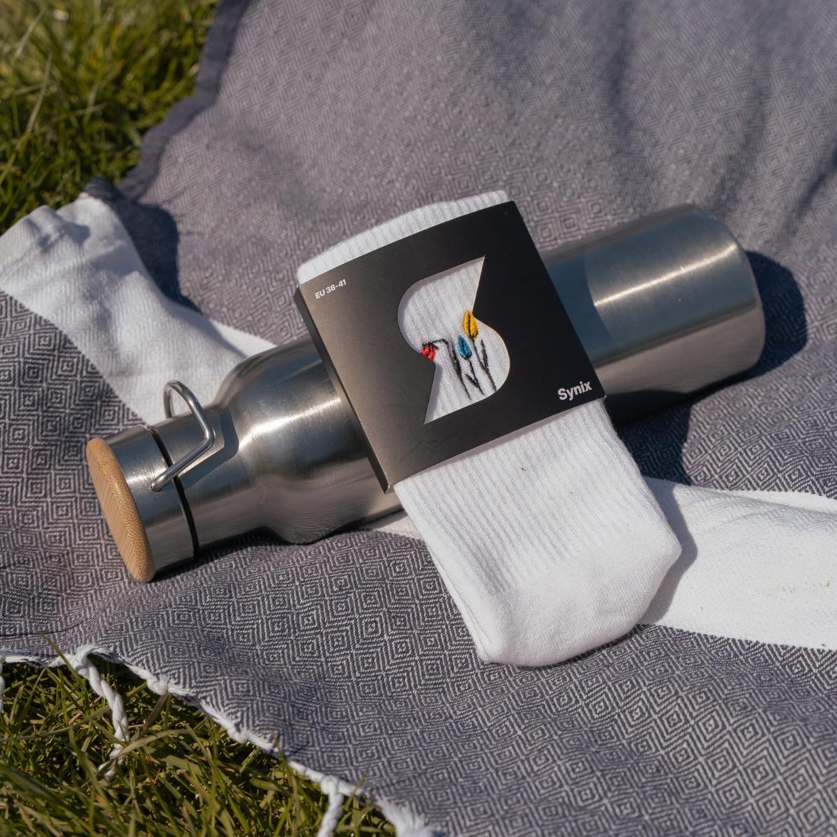 Close-up of colorful tulip embroidery on white Synix UnFold sock with packaging on picnic blanket